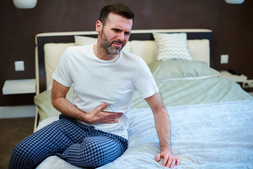 a man is sitting on a bed holding his stomach in pain