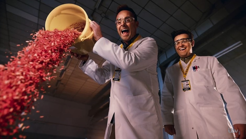 two men in lab coats are pouring something into a yellow bucket