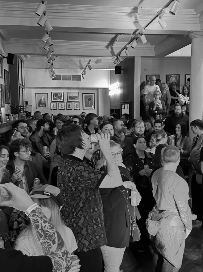 a crowd of people are gathered in a room with a few pictures on the wall