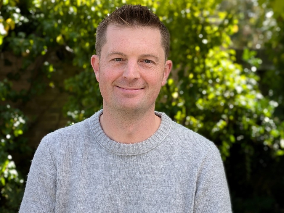 a man in a grey sweater smiles for the camera