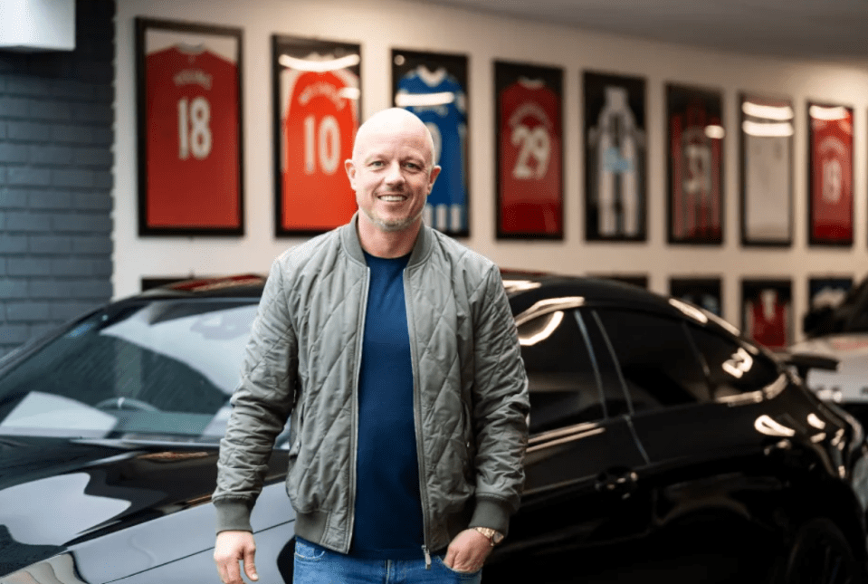 a man in a grey jacket stands in front of a black car