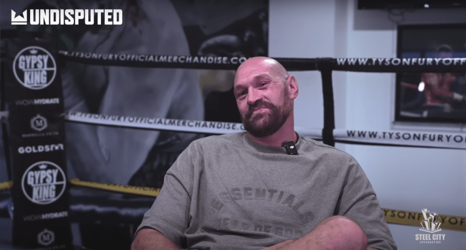 a bald man is sitting in front of a gypsy king sign