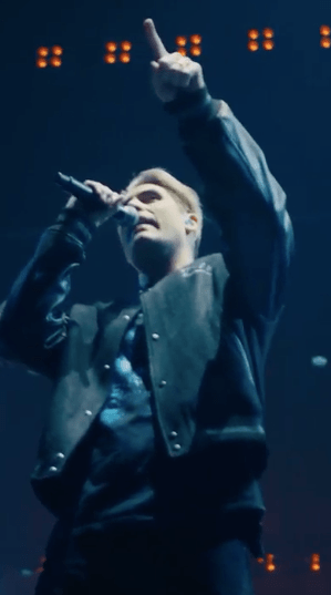 a man singing into a microphone with his hand in the air