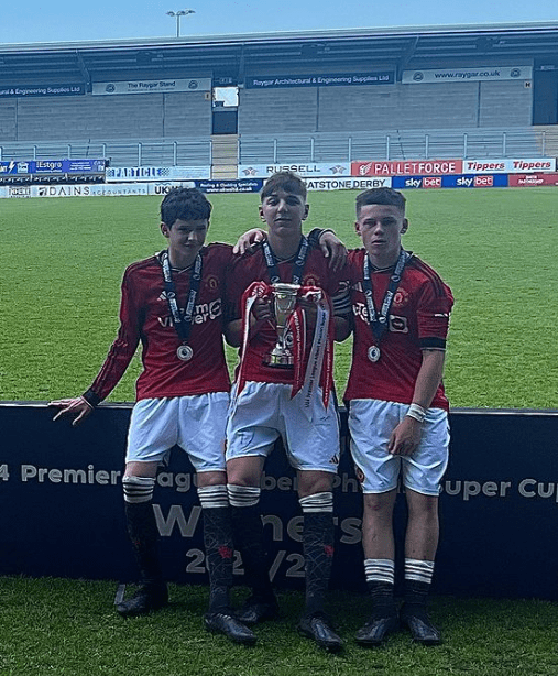 three soccer players holding a trophy in front of a sign that says premier league