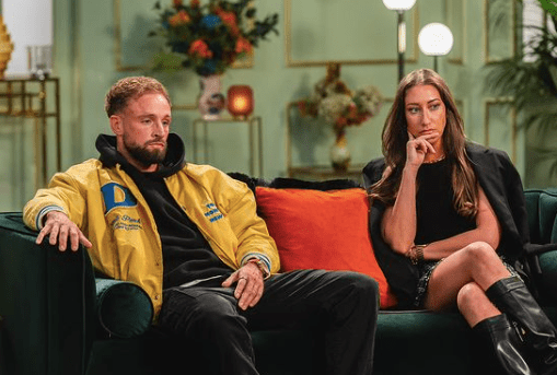 a man and a woman are sitting on a couch . the man is wearing a yellow jacket .