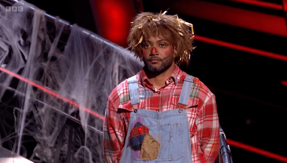 a man in overalls and a scarecrow costume stands in front of a bbc logo