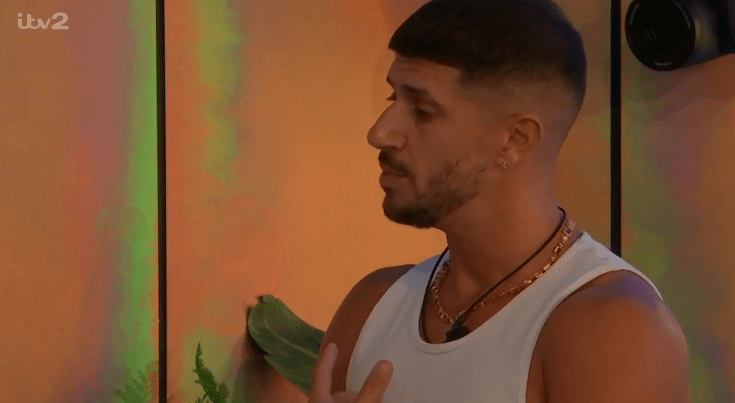 a man in a white tank top stands in front of a wall with itv2 written on it