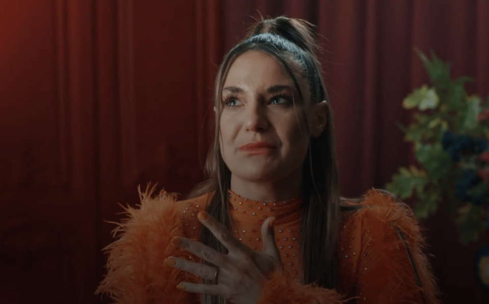 a woman wearing an orange feathered top is crying