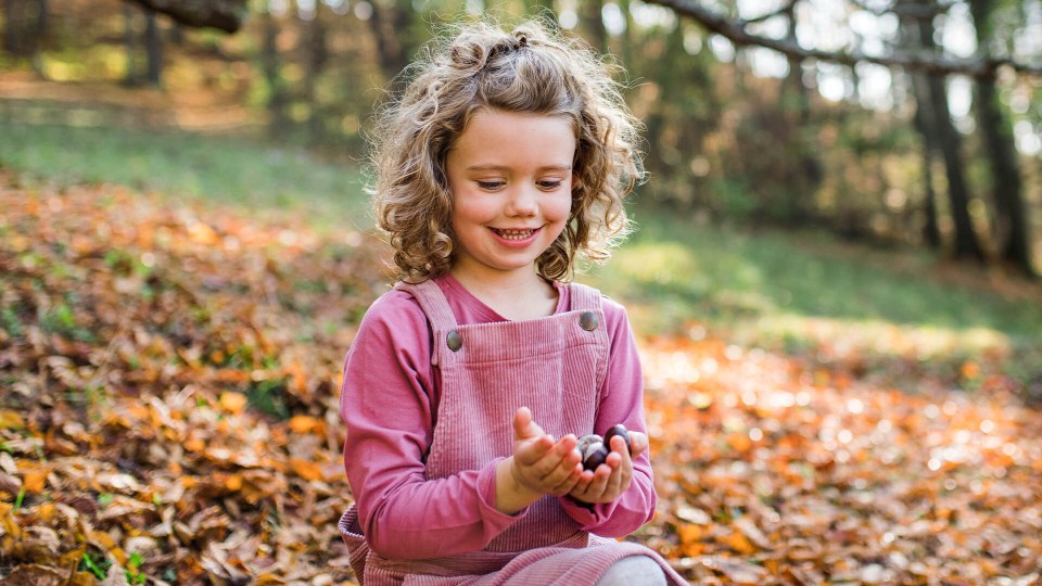 a little girl in pink overalls is holding berries in her hands