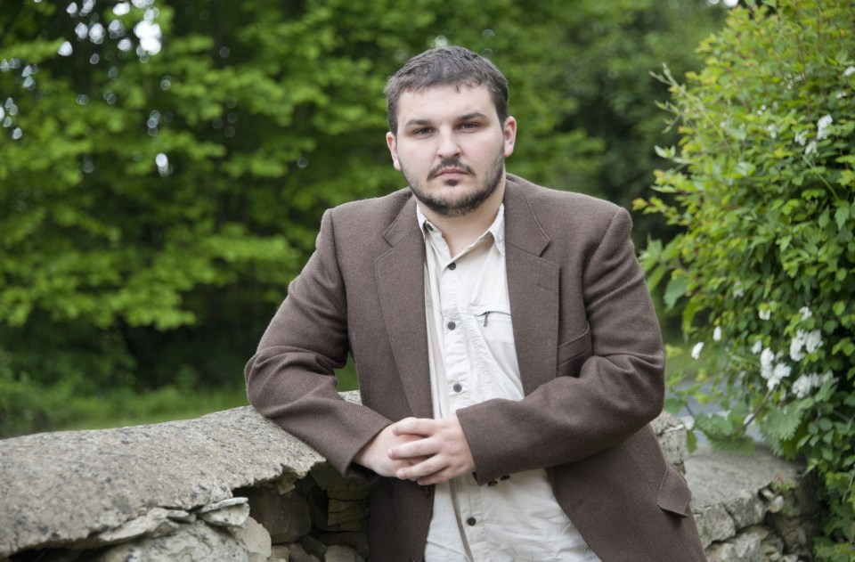 a man in a suit leans against a stone wall