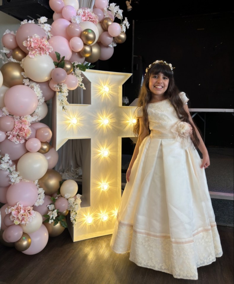 a little girl in a white dress stands in front of a large letter f