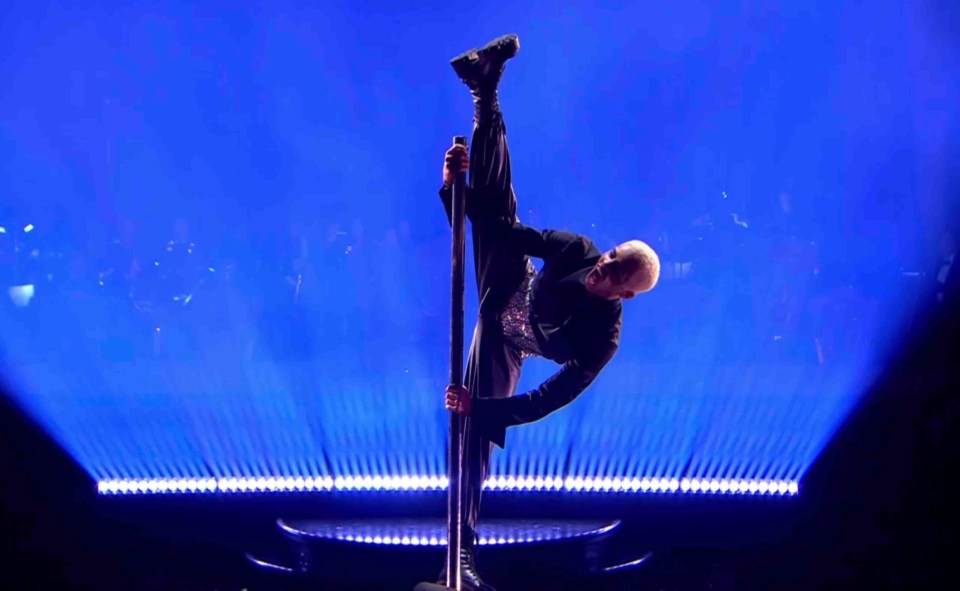 a man is doing a split on a pole in front of a blue background