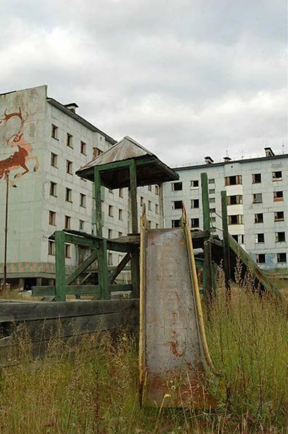 a slide sits in the grass in front of an abandoned building