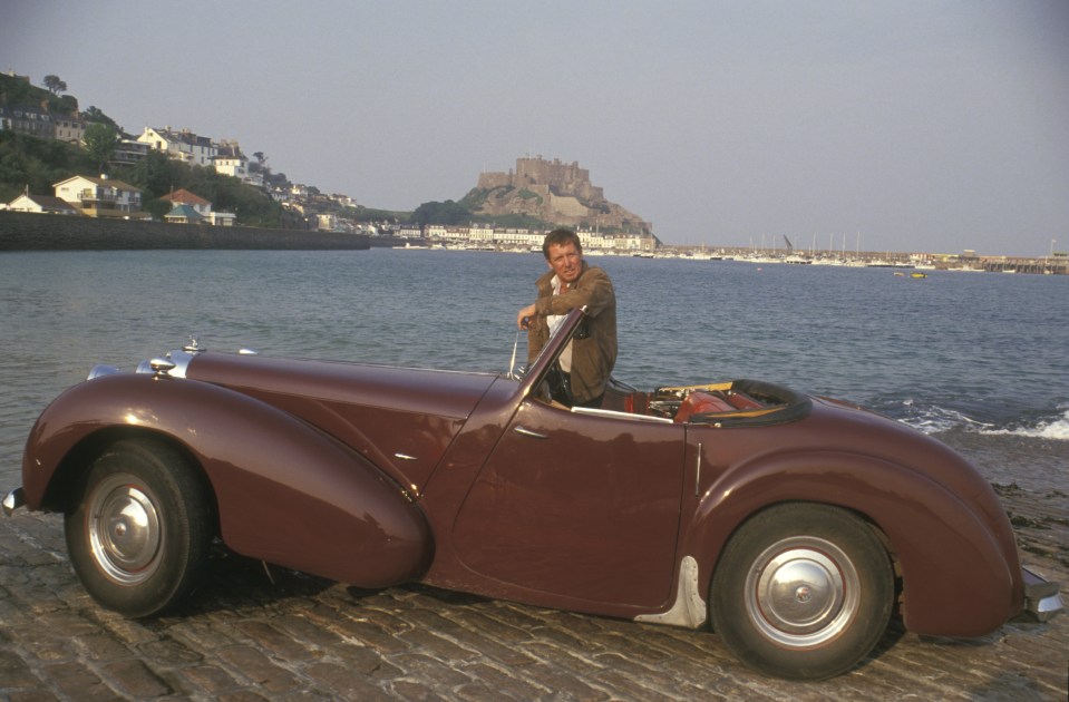 a man leans on a car with a castle in the background