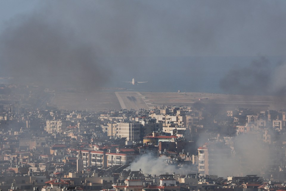 An airplane takes off at Beirut-Rafic Hariri International Airport as smoke rises over Beirut’s southern suburbs after a strike