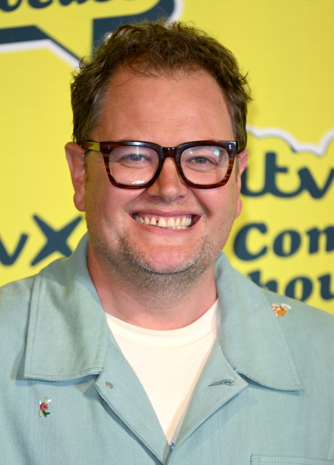 a man wearing glasses is smiling in front of a yellow sign that says itv