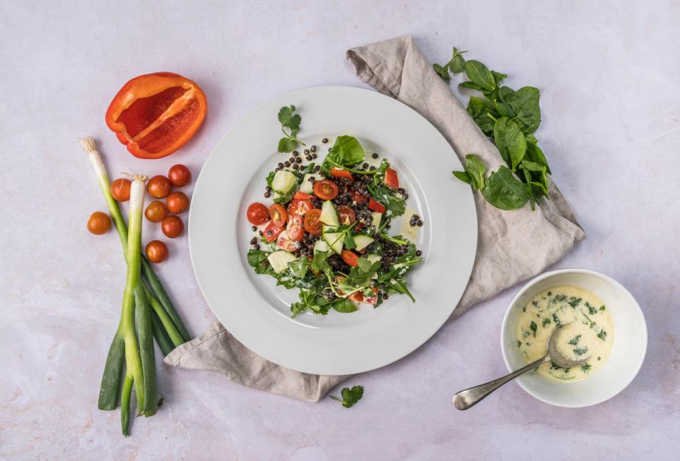 a white plate with a salad on it next to a bowl of dressing