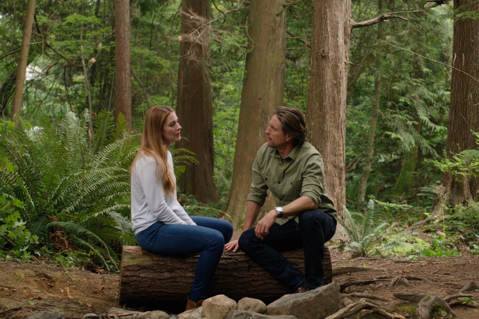 a man and a woman sit on a log in the woods