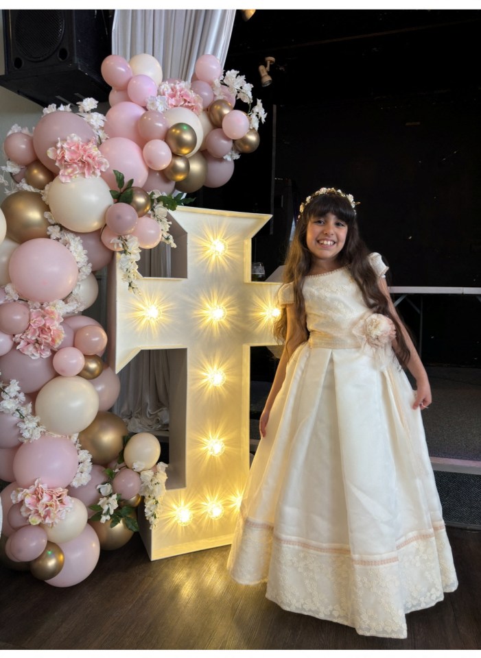 a little girl in a white dress stands in front of a large letter f