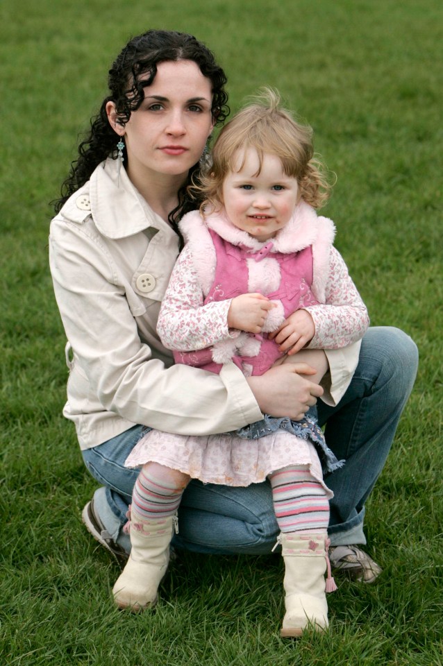 a woman kneeling down holding a little girl wearing a pink vest