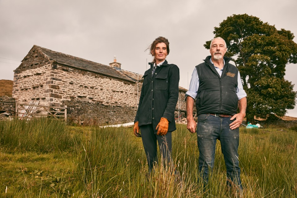 a man and a woman are standing in a field in front of a stone building