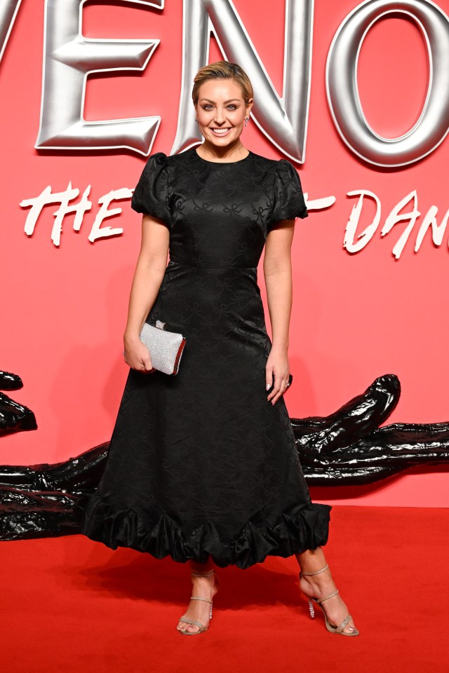 a woman in a black dress stands on a red carpet in front of a venom sign