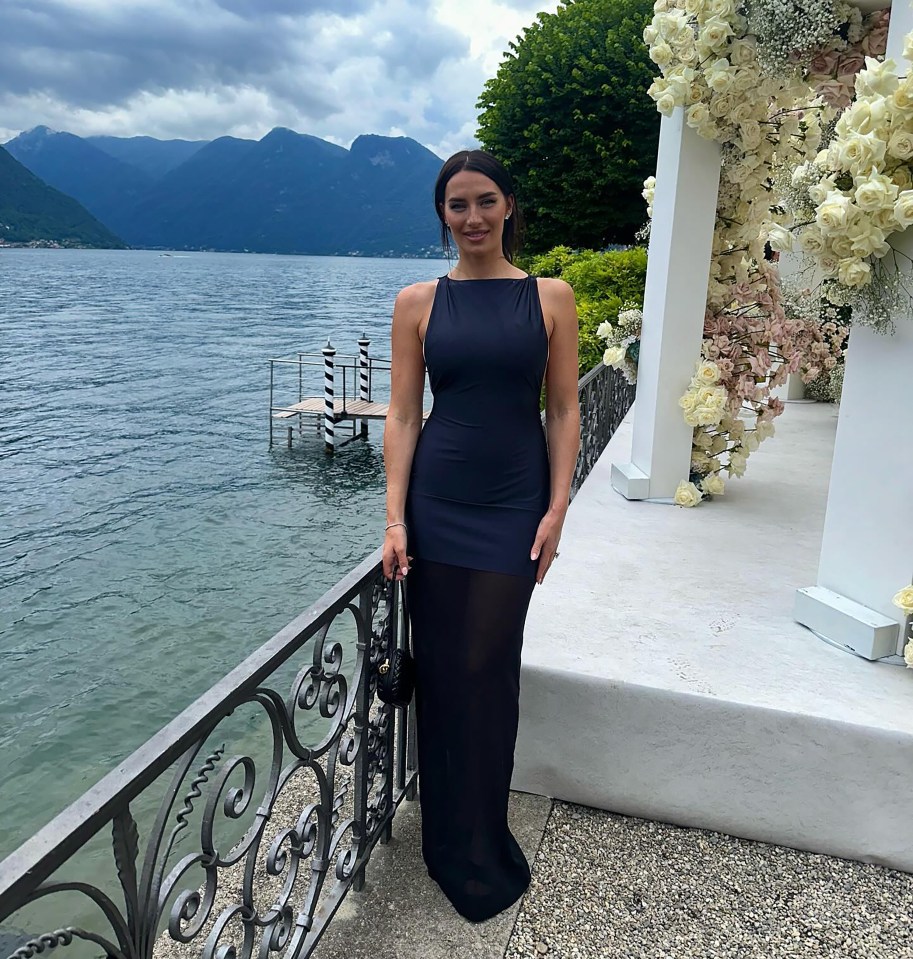 a woman in a black dress stands in front of a lake