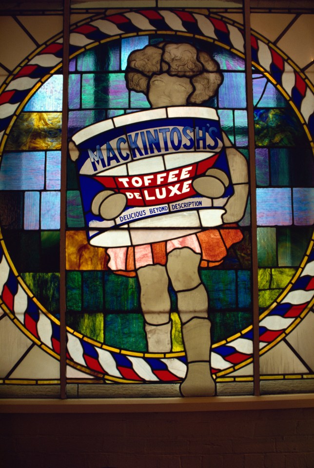 a stained glass window shows a person holding a can of mackintosh 's toffee deluxe