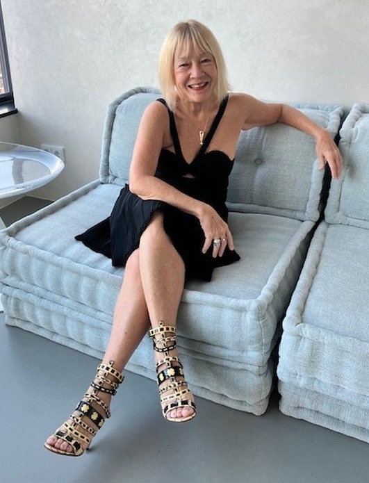 a woman in a black dress sits on a couch with her legs crossed