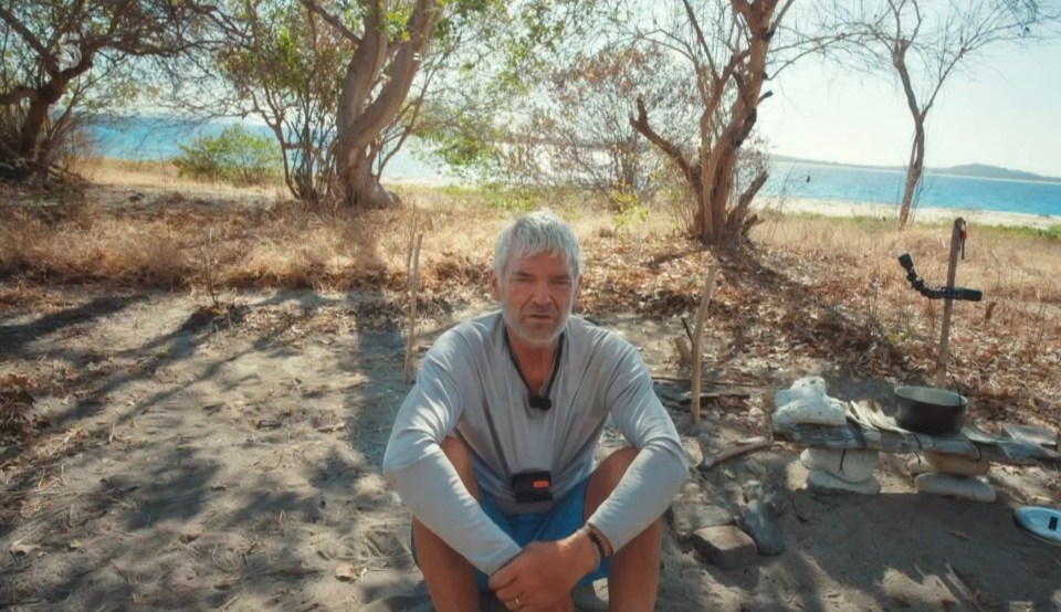 a man sits on a sandy beach with a camera around his neck