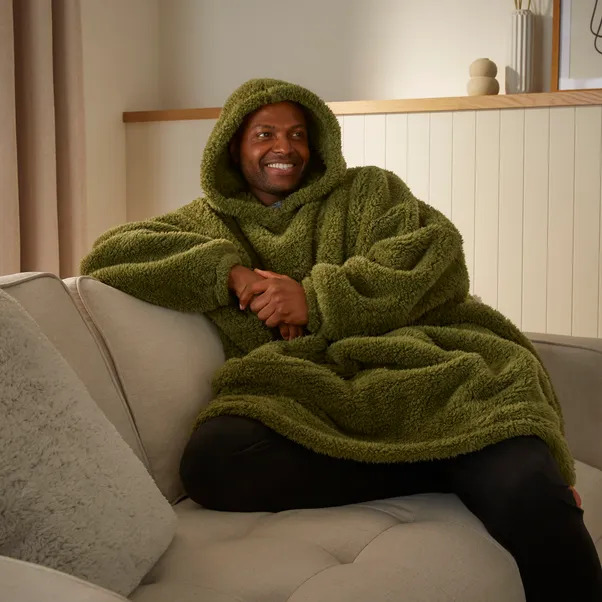 a man is sitting on a couch wearing a green blanket with a hood