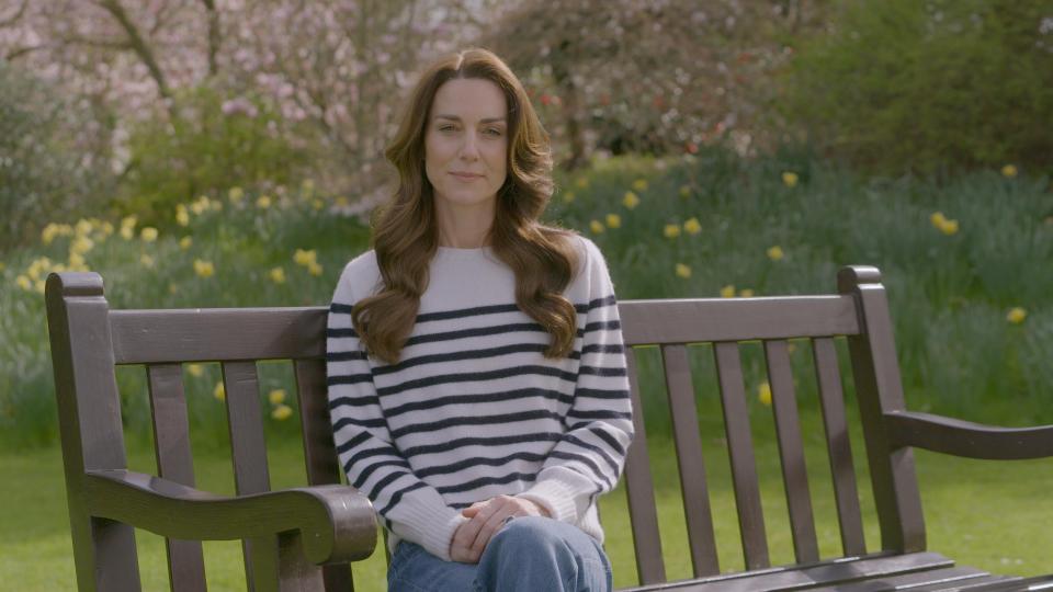 a woman in a striped sweater sits on a park bench