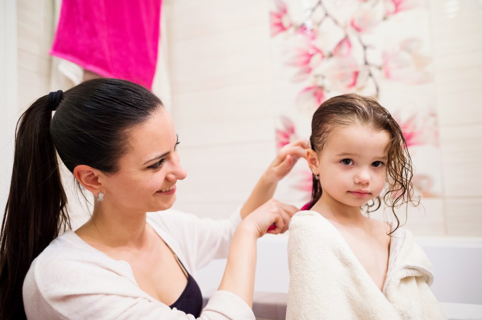 a woman brushing a little girl 's hair in a bathroom