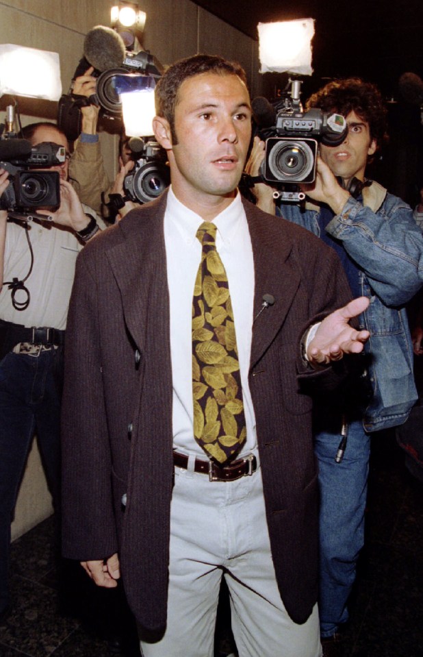 a man in a suit and tie is surrounded by cameras and microphones