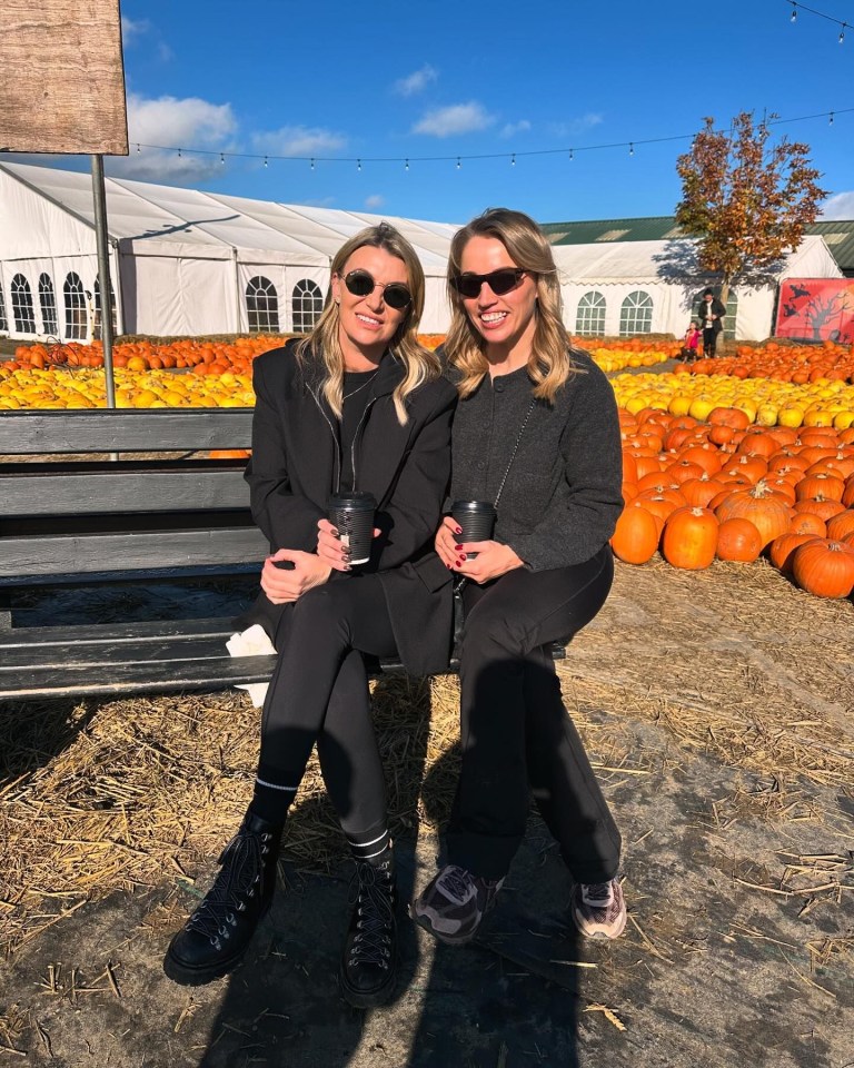 two women sit on a bench in front of a field of pumpkins