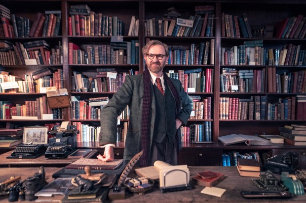 a man stands in front of a bookshelf with a sign on it that says ' william ' on it