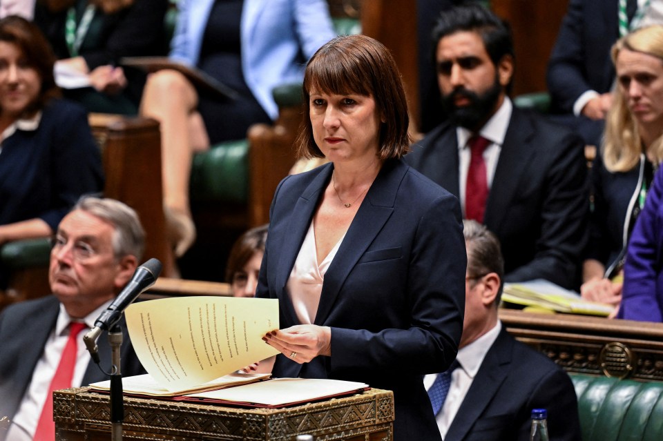 a woman in a suit stands at a podium holding a piece of paper