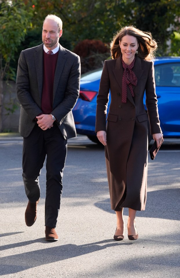 a man in a suit and a woman in a brown coat walk down a street