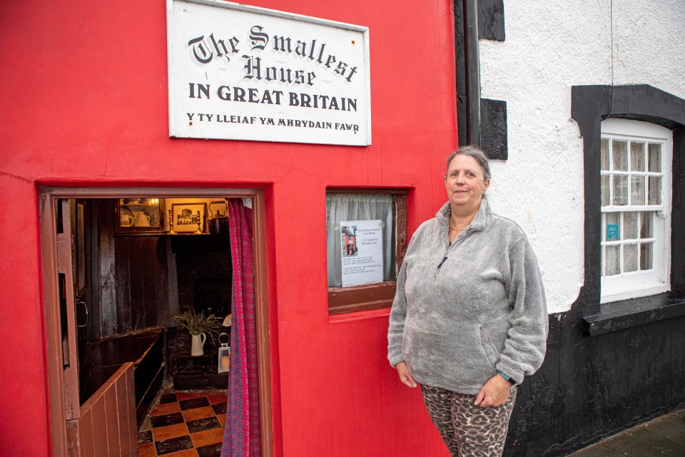 a woman stands in front of the smallest house in great britain