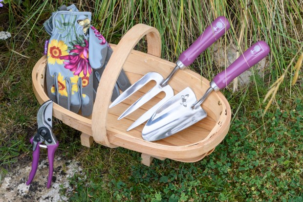 a wooden basket filled with gardening tools including a pair of gloves