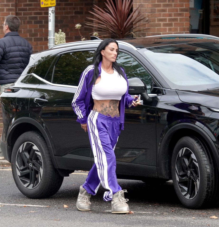 a woman in purple pants and a white crop top walks towards a black car