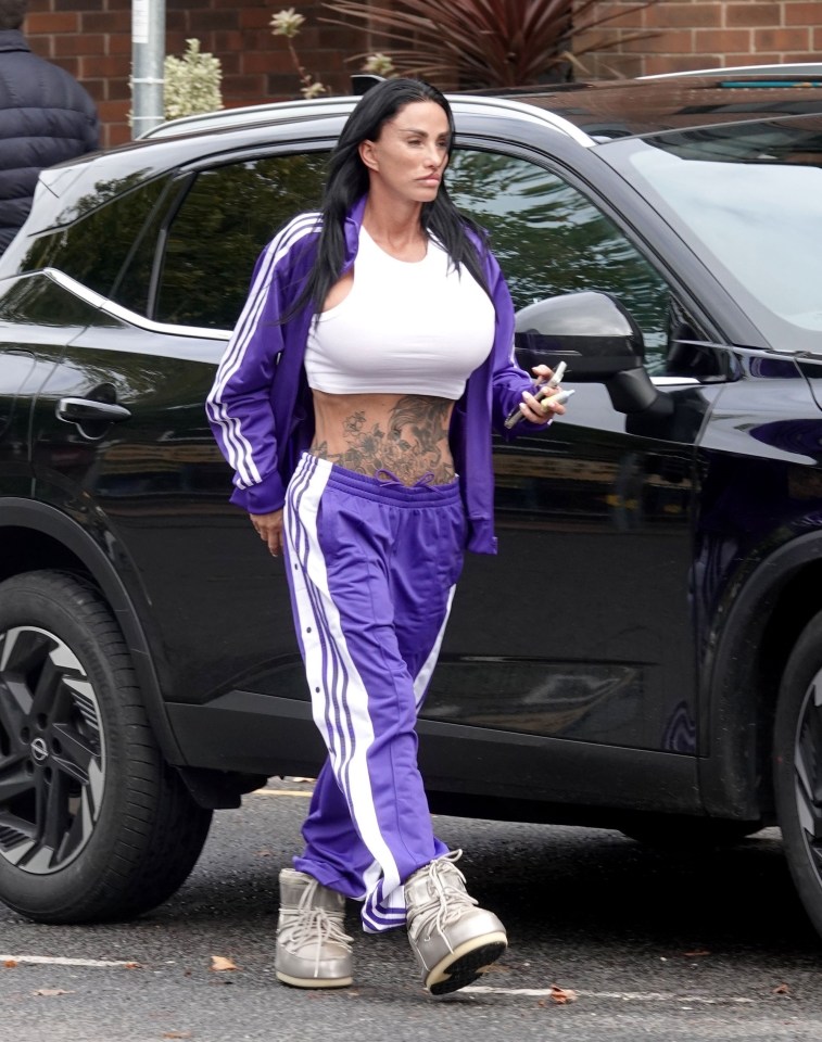 a woman in purple sweatpants and a white crop top is standing in front of a black car