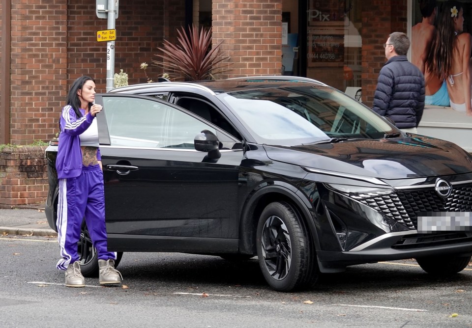 a woman in purple pants stands next to a black nissan car