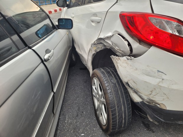 a white car with a damaged fender is parked next to a silver car