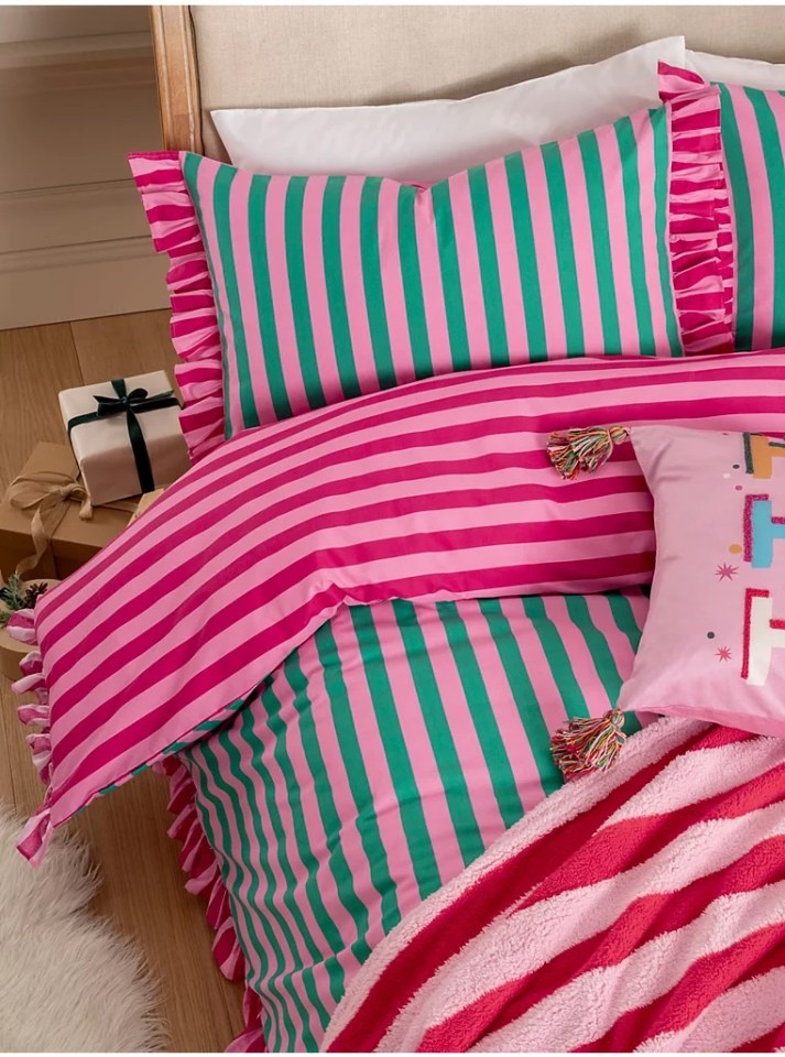 a bed with a pink and green striped comforter and pillows