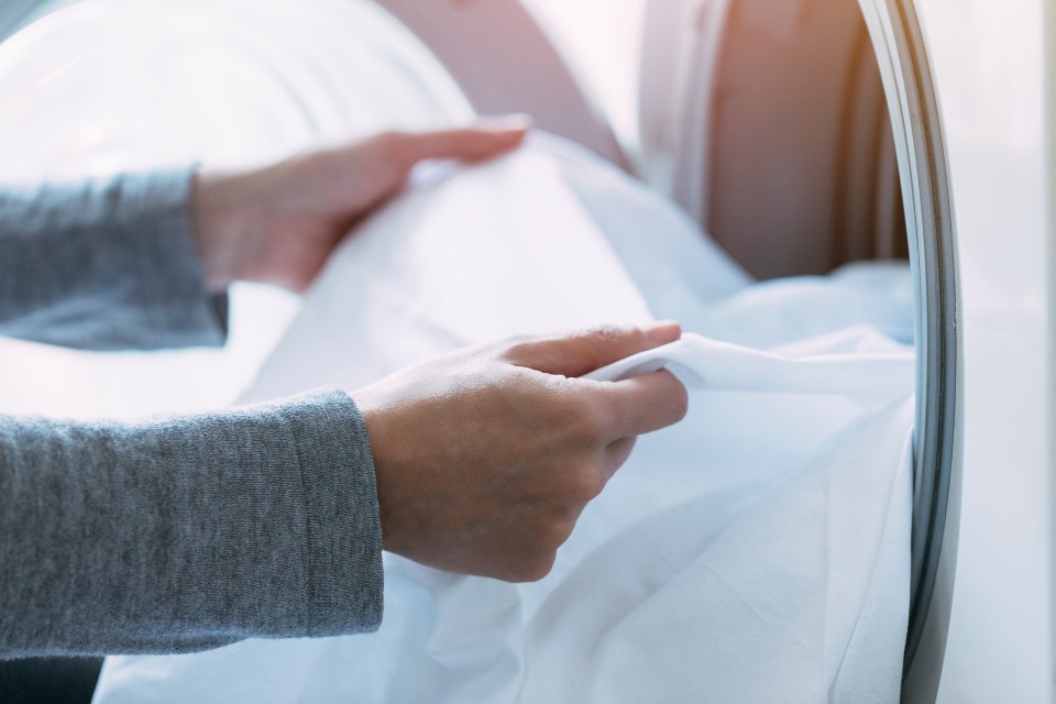 a person is putting white sheets into a washing machine