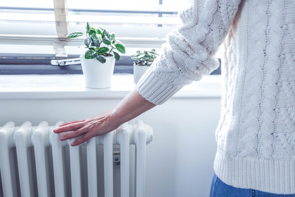 a woman in a white sweater is touching a radiator