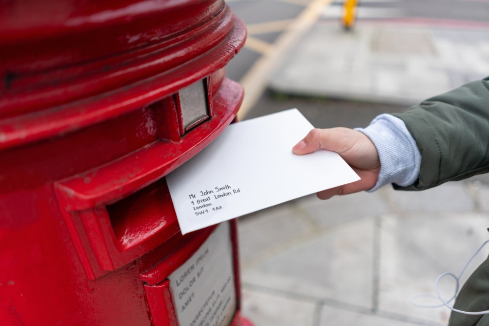 a person is putting an envelope in a red mailbox addressed to john smith