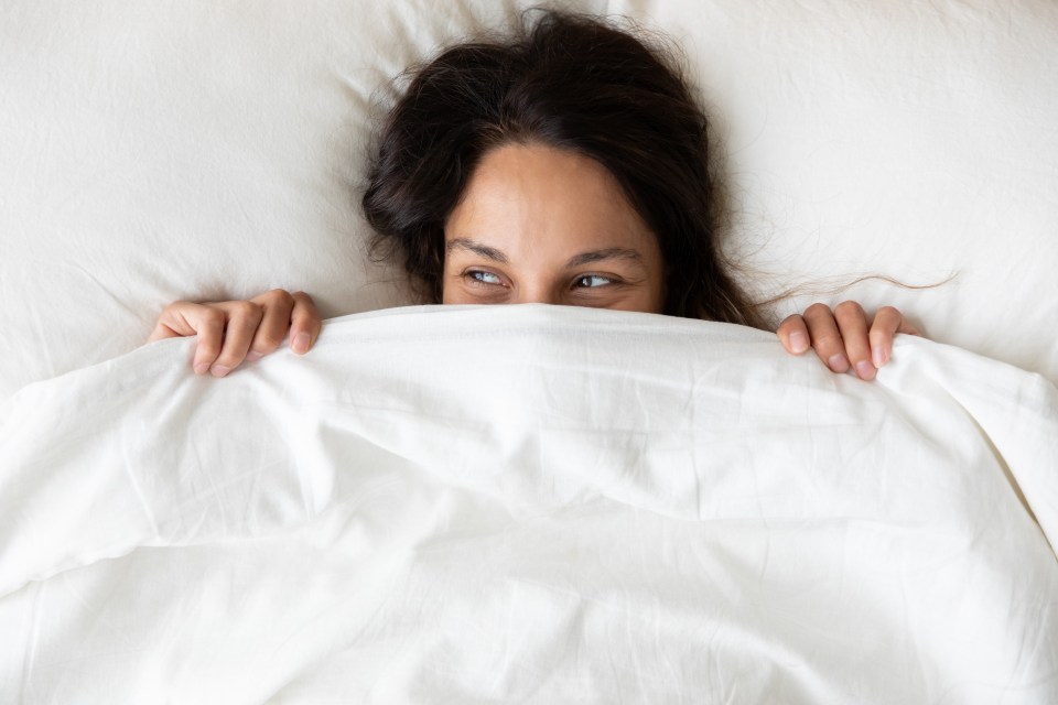 a woman peeking out from under a white blanket