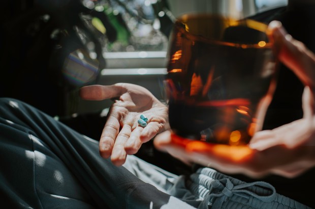 a person is holding a glass and a pill in their hand